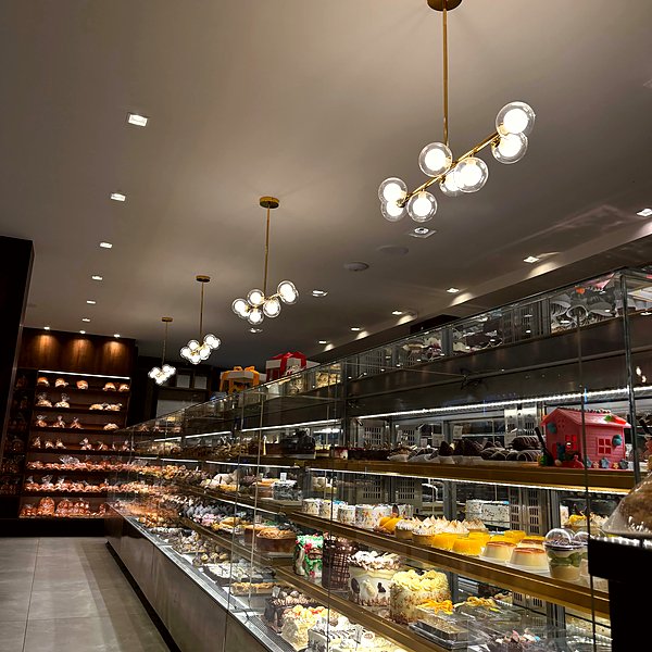 Vitrine de bolos e doces artesanais da Gentil Panificadora com luminarias modernas